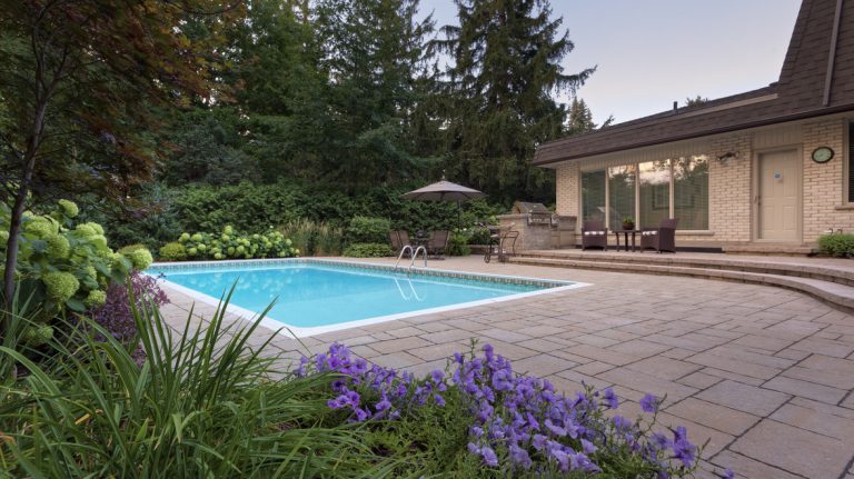 An inground pool with a surrounding stone patio and an outdoor kitchen.