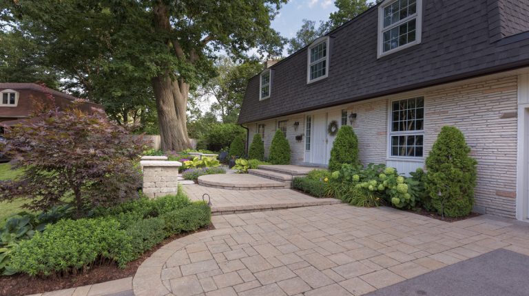 A front patio with driveway pavers and a garden on either side of the walkway that leads to the front door.
