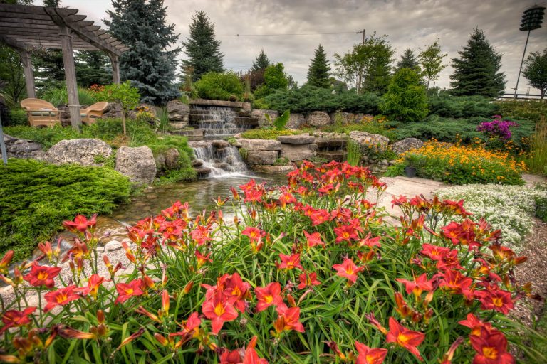 A multilevel landscape with a waterfall and a variety of flowers and bushes.