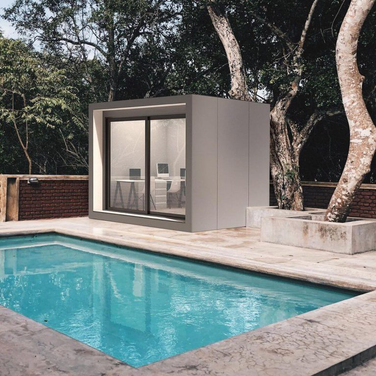 A stand-alone office room sits outside on a stone patio near an inground pool.