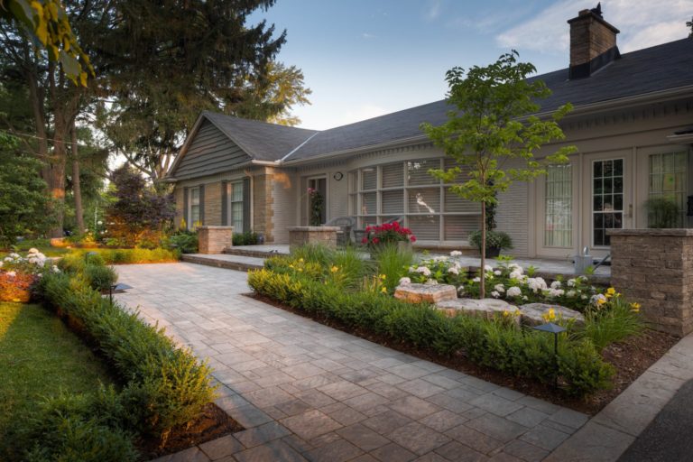 A stone walkway leads to the steps of a large front patio. It is lined by small bushes and two separate gardens