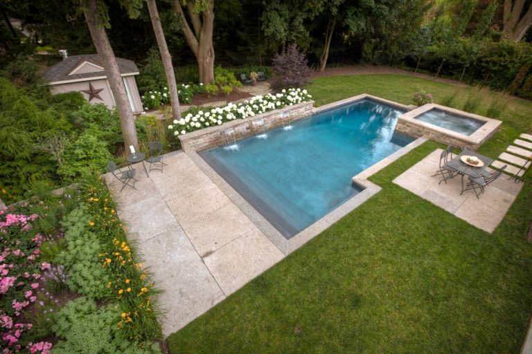 Pool with beautiful waterfall features and adjoining hot tub, flower bed, and stone patio.