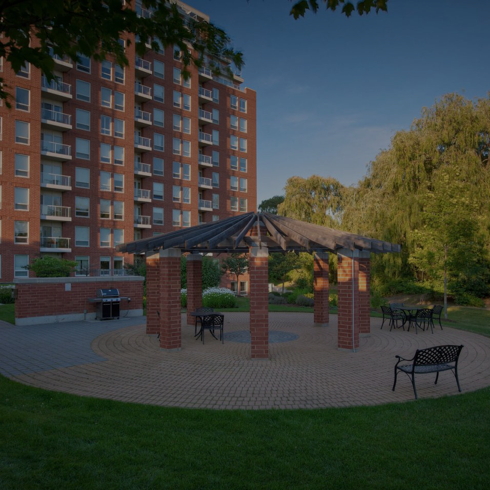A resting area outside an apartment building with a pergola and interlocking bricks.