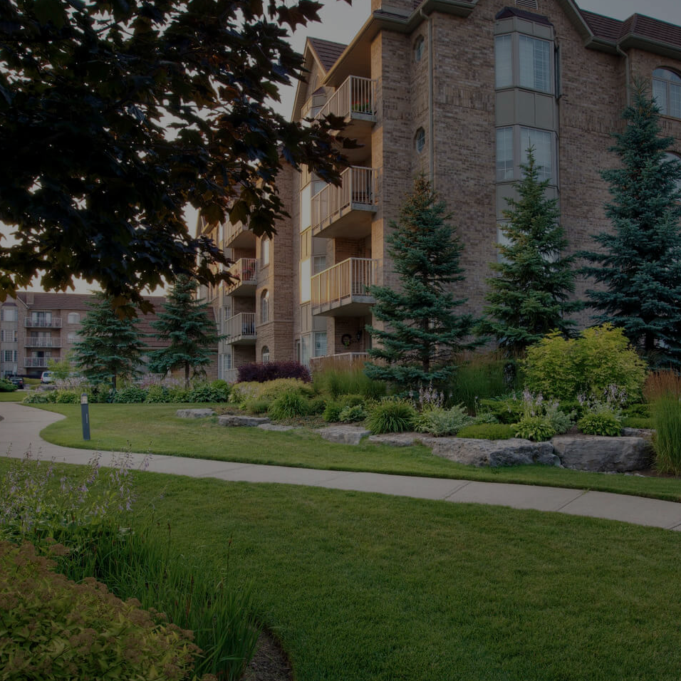 A long sidewalk curves through beautiful landscaping and gardens alongside a retirement home.