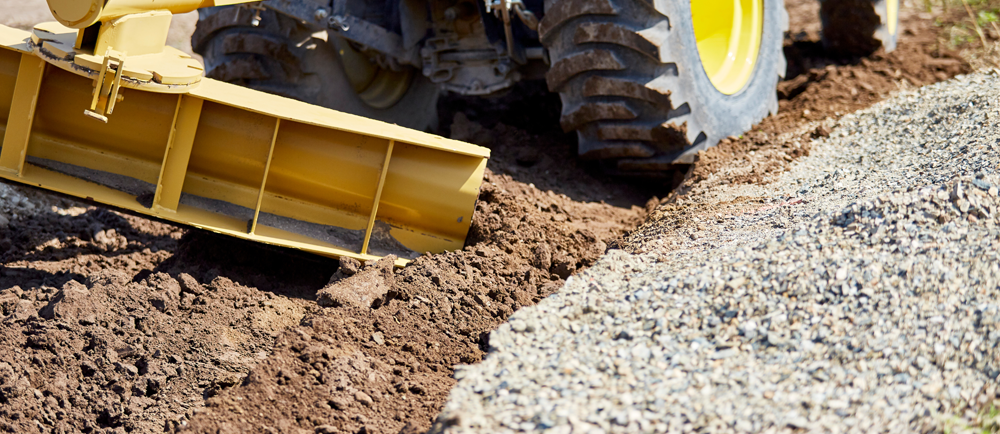 grading-and-drainage a machine pushing dirt along side gravel