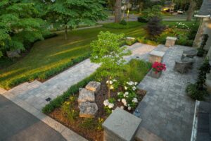 A beautifully landscaped garden features a stone walkway, vibrant flowers, and lush greenery, bordered by trees and hedges in a tranquil setting.